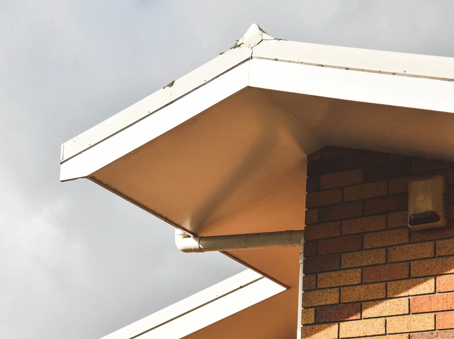 corner of roof with gutter with side brick wall and grey clouds behind the building