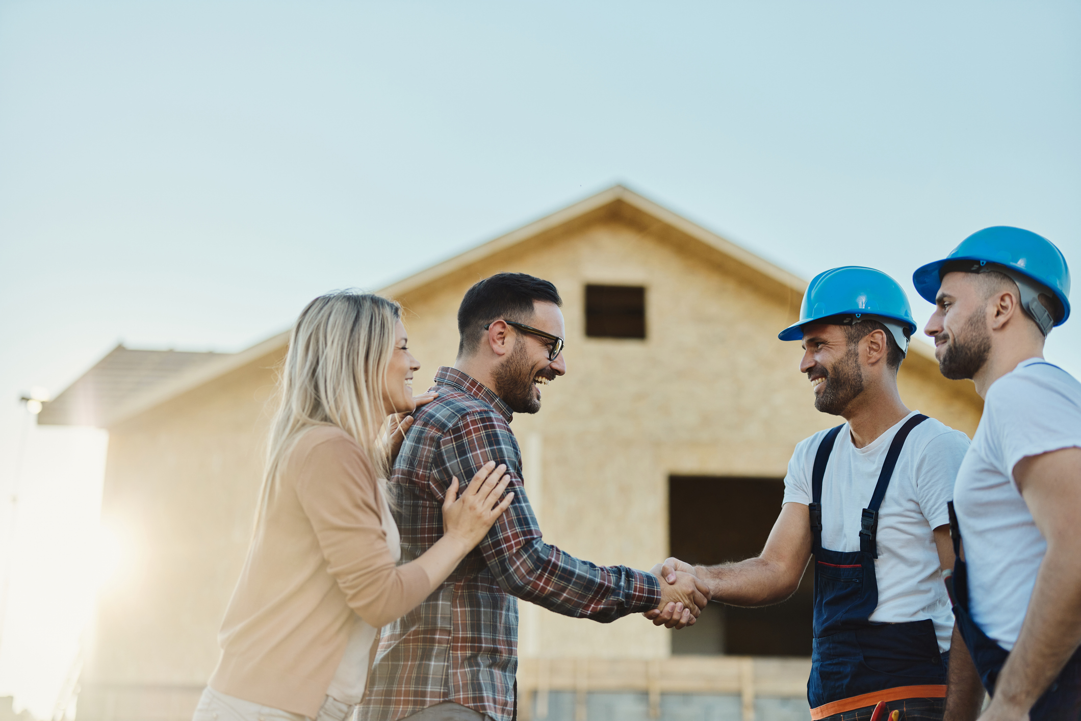 A happy couple shaking construction workers hands in front of their rebuilding house