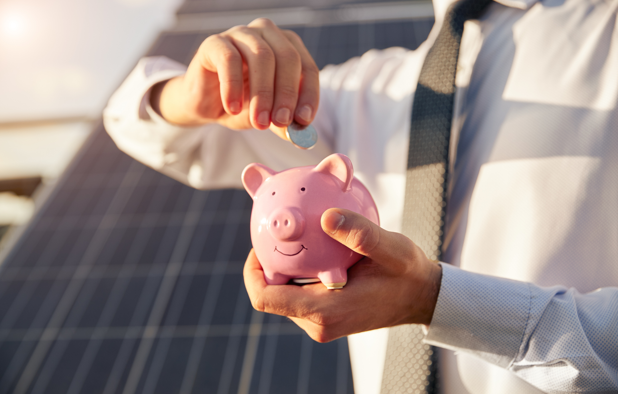 man-putting-money-into-a-piggy-bank-near-solar-panel